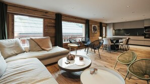 Ein modernes Wohnzimmer mit Sofa, Couchtisch und Sesseln. Es gibt eine Küchenzeile mit Esstisch und Stühlen.