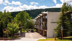 A hotel with multiple balconies, a parking area, and a sign for a shuttle service. - Lichenhearth 25 (Snowmass Village)