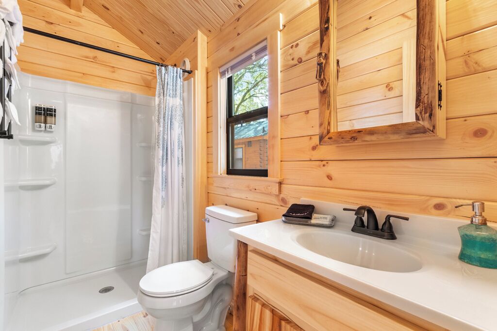 A wooden cabin bathroom with a toilet, sink, and shower.