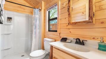 A wooden cabin bathroom with a toilet, sink, and shower.