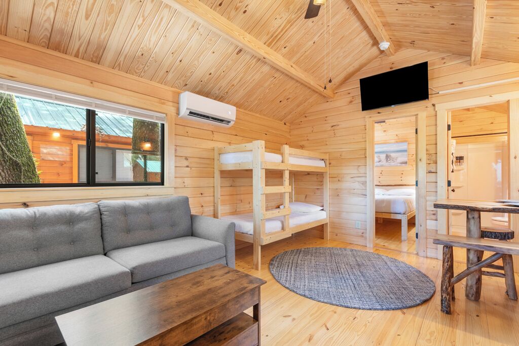 A cozy cabin with a gray sofa, bunk beds, a wooden table, and a TV.