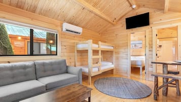 A cozy cabin with a gray sofa, bunk beds, a wooden table, and a TV.