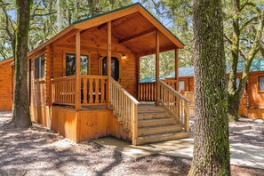 A wooden cabin with a porch and stairs, surrounded by trees.