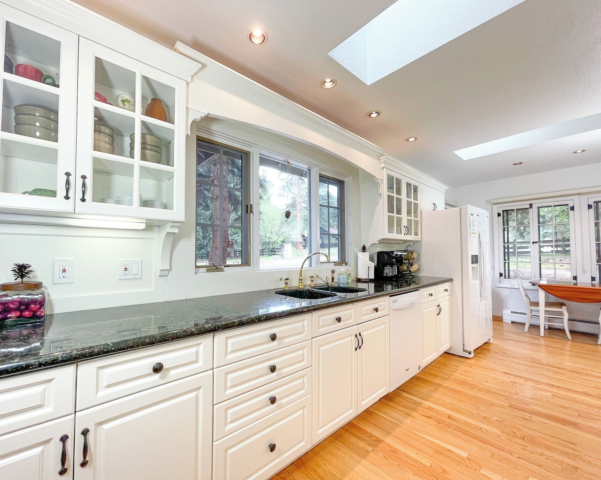 A spacious kitchen with white cabinetry, a black countertop, and a large window.