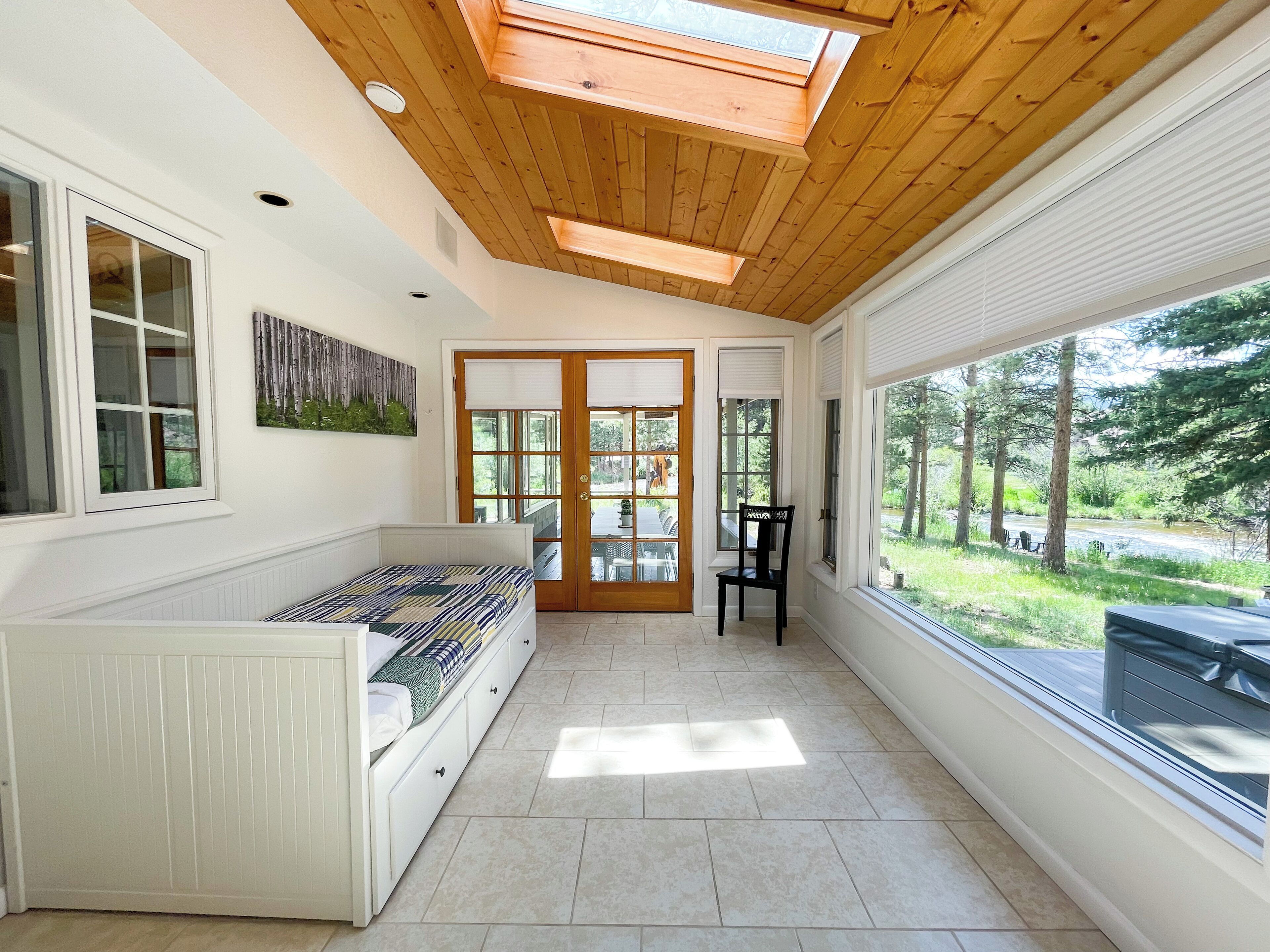 A room with a skylight, a bed, a chair, and a view of a garden.