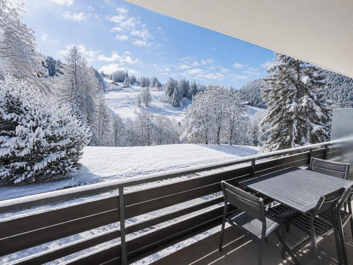 A balcony with a view of a snow-covered landscape and a table with chairs.