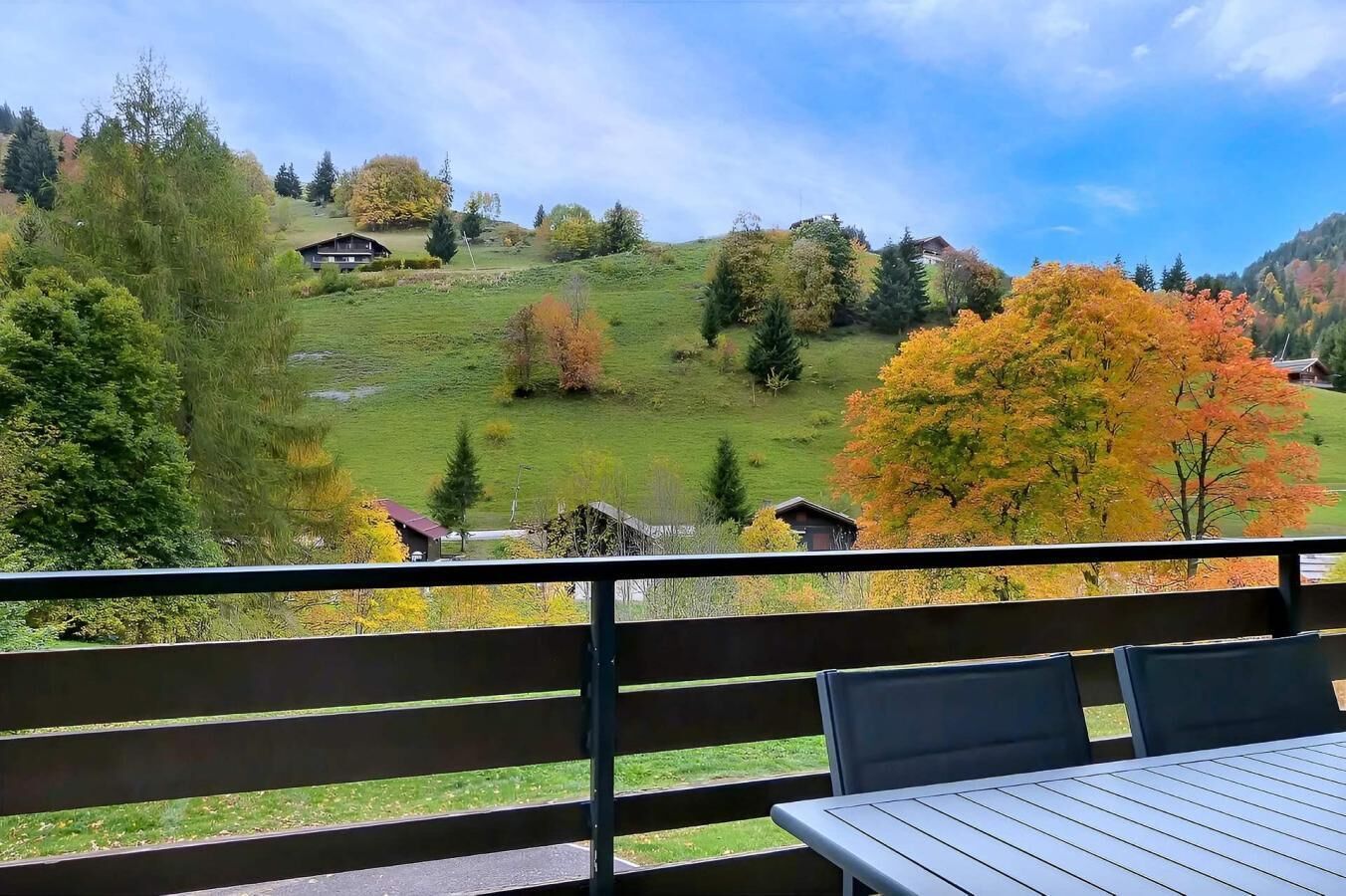 Ein Balkon mit Tisch und Stühlen, der einen Blick auf einen Hügel mit Häusern und Bäumen bietet.