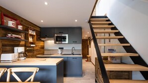 Una cocina moderna con una isla central, estantes de madera y una escalera que sube a un nivel superior.