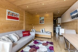 Ein gemütliches Blockhaus-Interieur mit einer Couch, einer Bank, einem Esstisch und einer Küchenzeile.