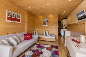 A cozy cabin interior with a sofa, a patterned rug, a small table with glasses and a pitcher, and wooden walls.