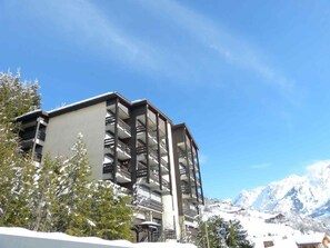 A multi-story building with balconies, surrounded by snow-covered trees and mountains in the background.