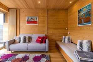A cozy room with a sofa, a bench, a colorful rug, wooden walls, and a poster. - 2nd floor, balcony, tv, ski locker, 27m², La Clusaz (La Clusaz)