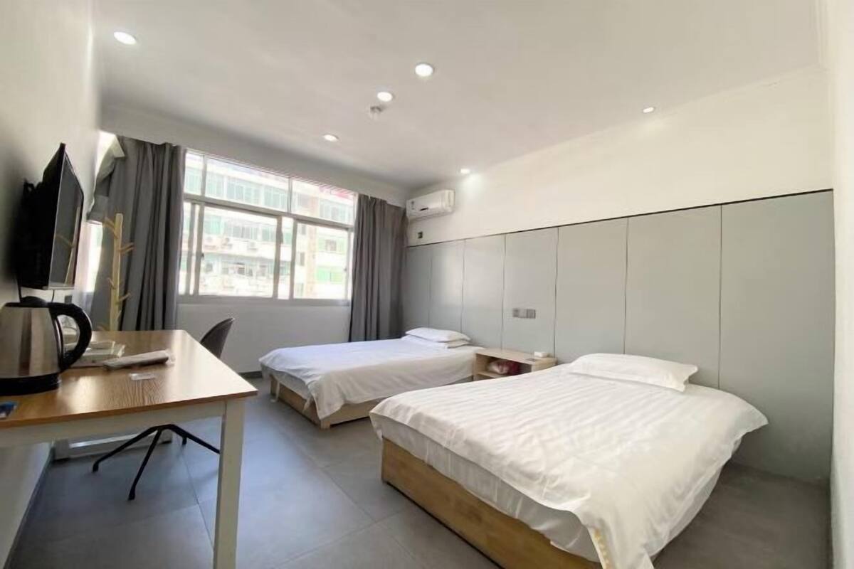 Habitación de hotel con dos camas individuales, un escritorio con hervidor, una silla y una ventana con cortinas.