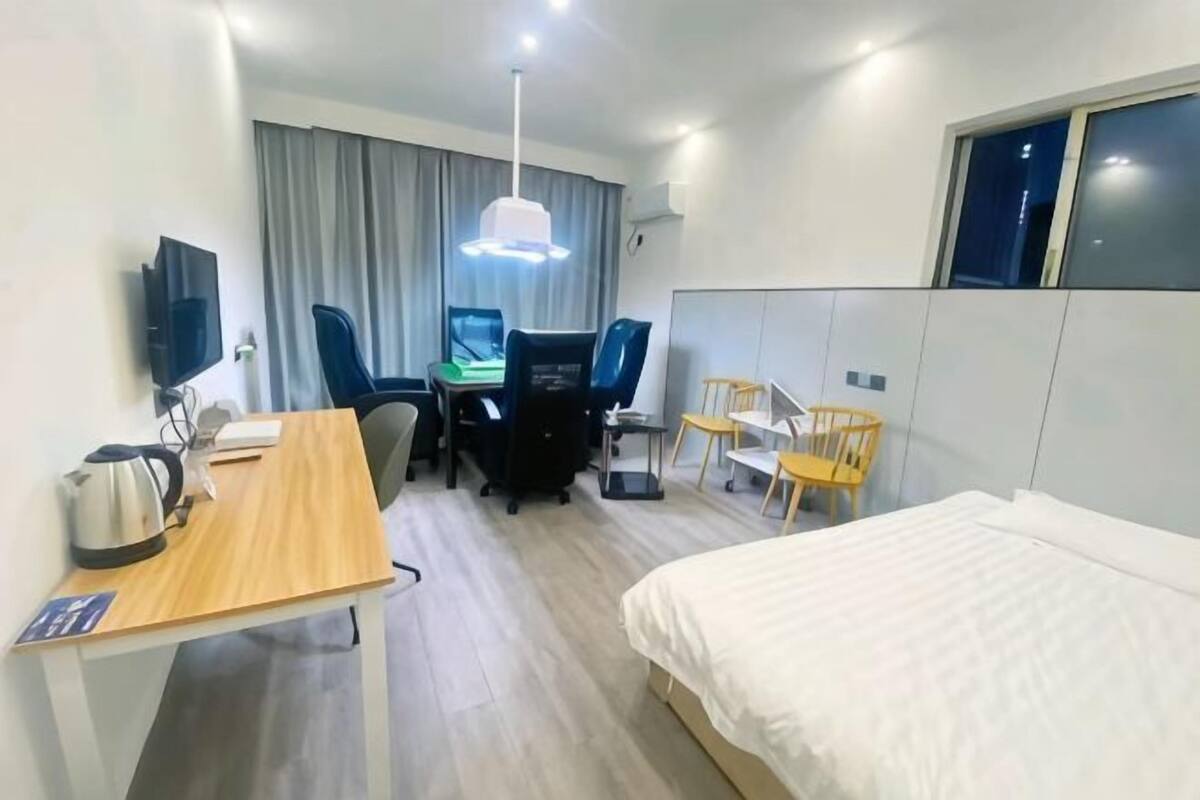 Habitación de hotel con cama, escritorio con hervidor, silla, mesa, televisor y ventana.