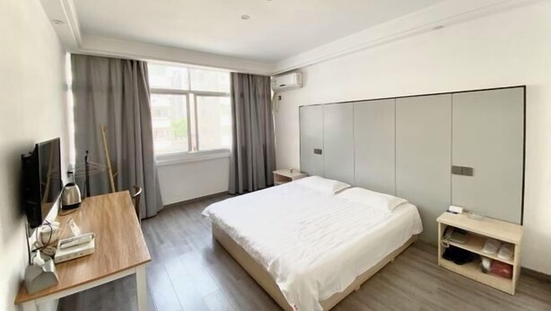 Een hotelkamer met een bed, een bureau met een computer, een televisie, een kledingkast en een raam met gordijnen.
