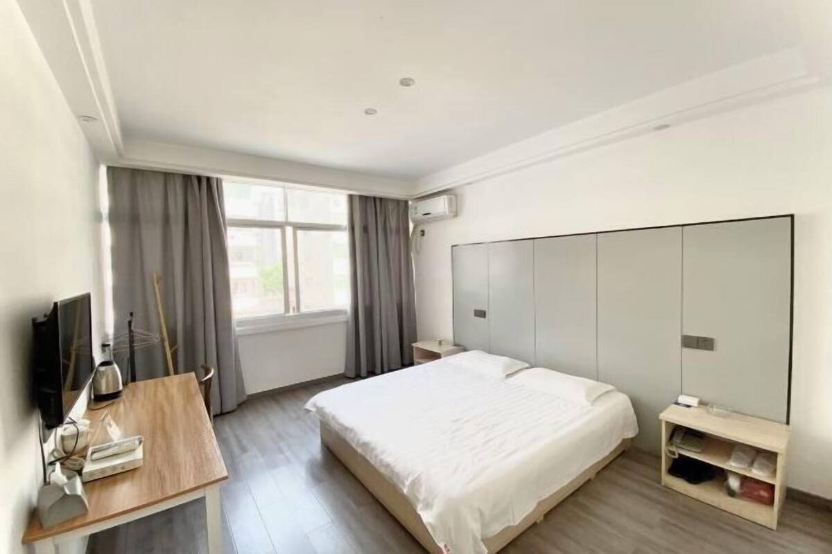 Habitación de hotel con cama, escritorio con computadora, televisión, armario y ventana con cortinas.