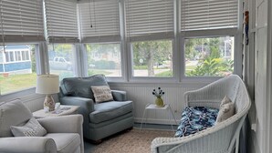 A room with a ceiling fan, two grey sofas, a wicker chair, a small table with a lamp, and a view of the outside. - 4-BdRm Home at Black Point Beach, East Lyme - WiFi + AC, Pet Friendly! (East Lyme)