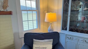 A blue armchair with a 'welcome home' pillow, a lamp, a window, and a cabinet with glass doors. - 4-BdRm Home at Black Point Beach, East Lyme - WiFi + AC, Pet Friendly! (East Lyme)