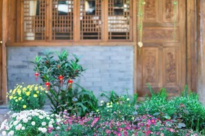 A traditional wooden door with a lattice window design, a brick wall, and a variety of colorful flowers in the foreground. - Home Inn (Zhongyi) (Lijiang)