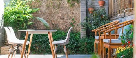 A patio with a table and chairs, surrounded by potted plants and a brick wall.