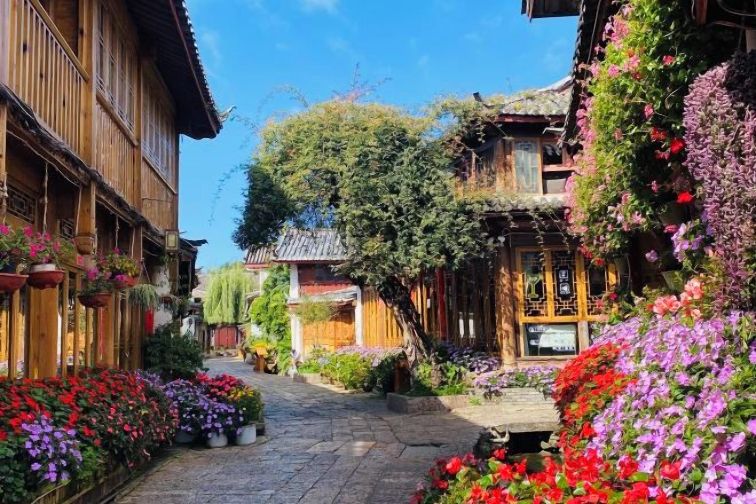 A narrow street with traditional wooden buildings, a cobblestone path, and vibrant flowers.