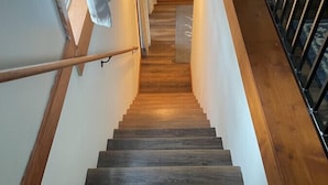 A wooden staircase with a handrail, leading to a landing with a light fixture.
