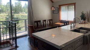 A spacious kitchen with a large island, a dining area with chairs, a balcony with a railing, and a view of the outdoors.