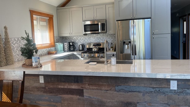A modern kitchen with grey cabinets, stainless steel appliances, and a herringbone tile backsplash.