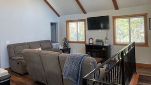 A living room with a sectional sofa, a flat-screen TV mounted on the wall, and a staircase with a wooden railing.