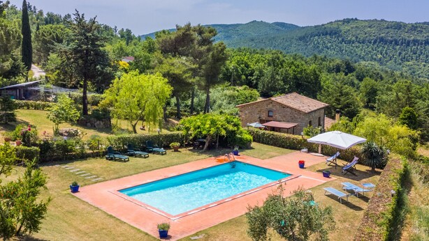 Une piscine entourée d’un jardin, avec un bâtiment en pierre et une vue sur les collines.