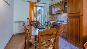 Une cuisine avec des meubles de rangement en bois, une table à manger avec des chaises et une vue sur l’extérieur.