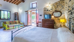 A bedroom with a bed, a dresser, a TV, and a stone wall. - Fienile by Interhome (Castelnuovo Val Cecina)