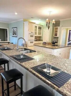 A kitchen with a granite countertop, two bar stools, a double sink, and a hanging light fixture. - 6BR Executive Home in Gated Golf Community – Sleeps 12 – 30-Day Minimum Stay (Montgomery)