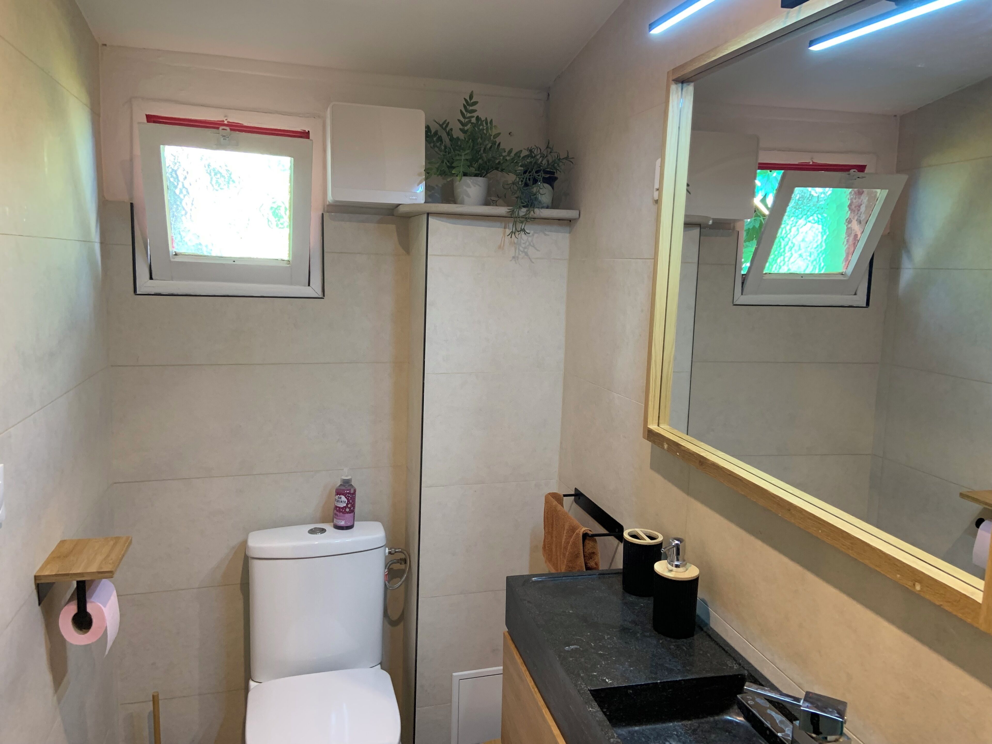 A bathroom with a toilet, sink, mirror, and a small window.