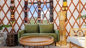 Una habitación con sofá verde, una mesita de mimbre y una pared decorativa con totems.