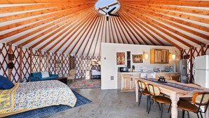 Una yurta con una zona de cocina, una mesa de comedor y una cama con colcha estampada.