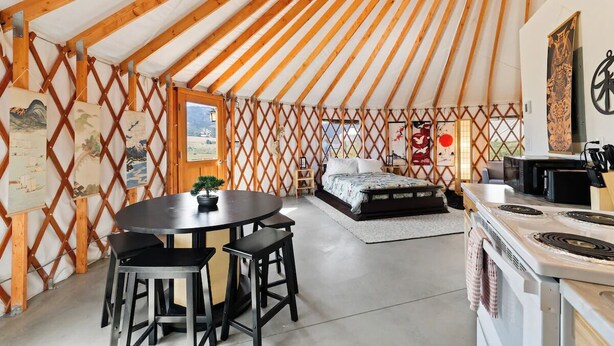 Una yurta acogedora con una cama, una zona de comedor con mesa y sillas, y una cocina con estufa.