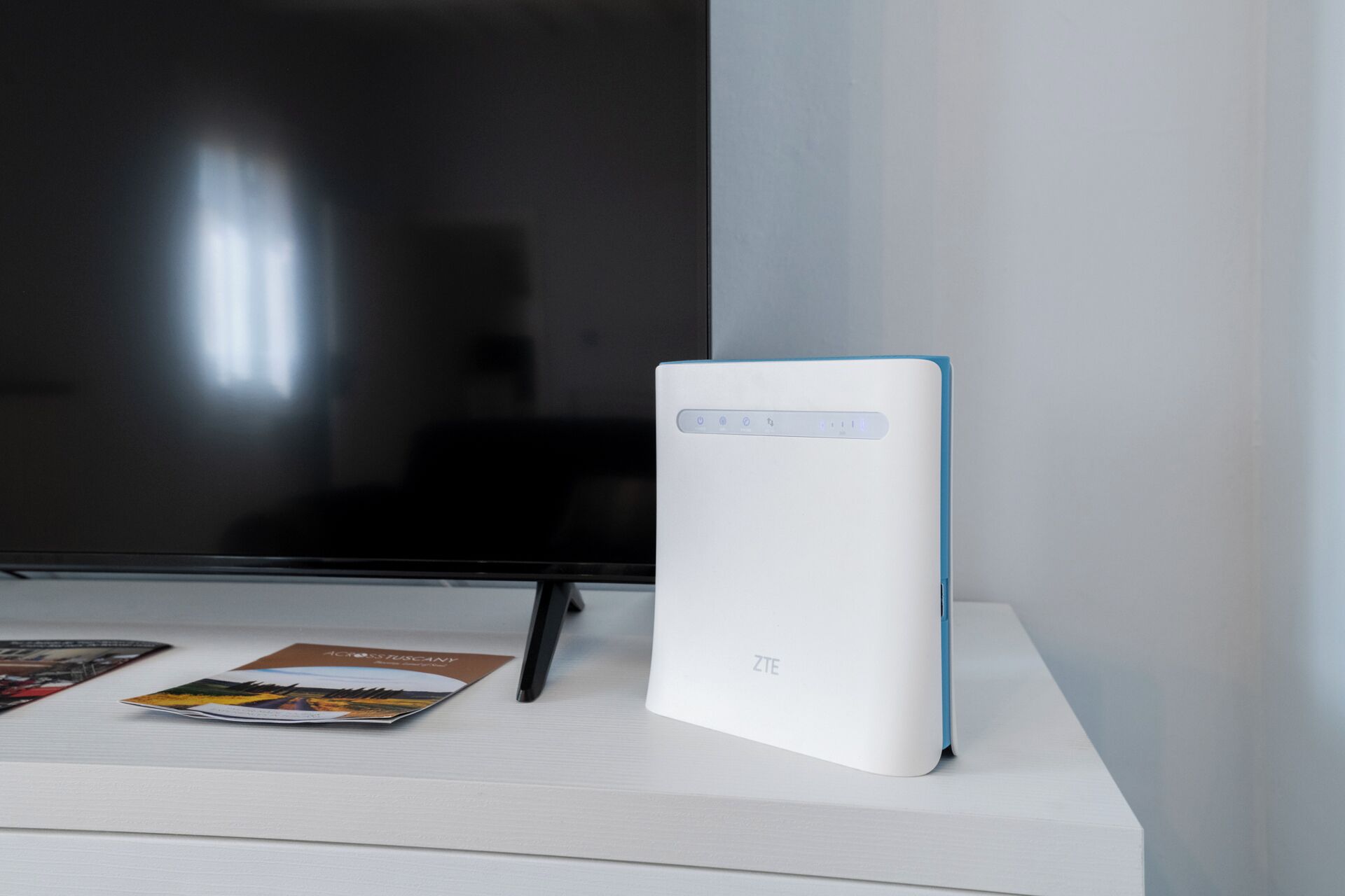 Un dispositivo ZTE blanco sobre una superficie blanca, con un televisor negro al fondo.