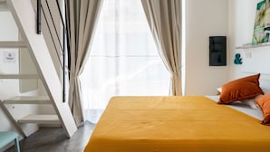 Un dormitorio con una cama, almohadas anaranjadas, una ventana con cortinas, una obra de arte en la pared y una escalera.