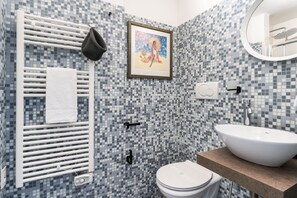 A bathroom with a mosaic tile wall, a white radiator, a framed artwork, a white sink, and a toilet.