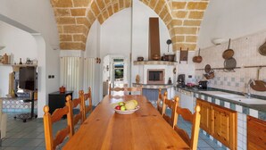 Una cocina amplia con techo de ladrillo abovedado, una larga mesa de madera con sillas y un bol de fruta sobre la mesa.