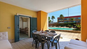 Un balcón con una mesa de comedor para cuatro personas, un sofá y vistas a una piscina y un edificio.