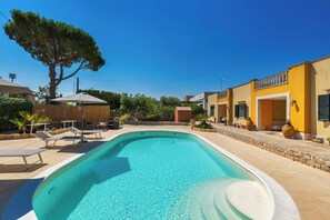 Una piscina con sillones de descanso, una pérgola de madera y edificios amarillos con balcones.