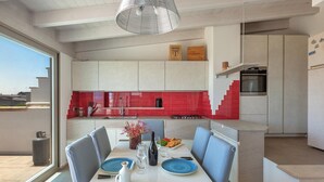 A modern kitchen with red and white cabinets, a dining area with blue plates, and a staircase leading to an upper level.