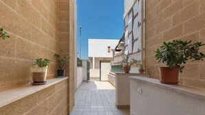 A narrow corridor with tiled flooring, potted plants on shelves, and a clear blue sky.