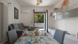 Un comedor con una mesa preparada para cuatro personas, un sofá y vistas a un área exterior con vegetación a través de un ventanal.