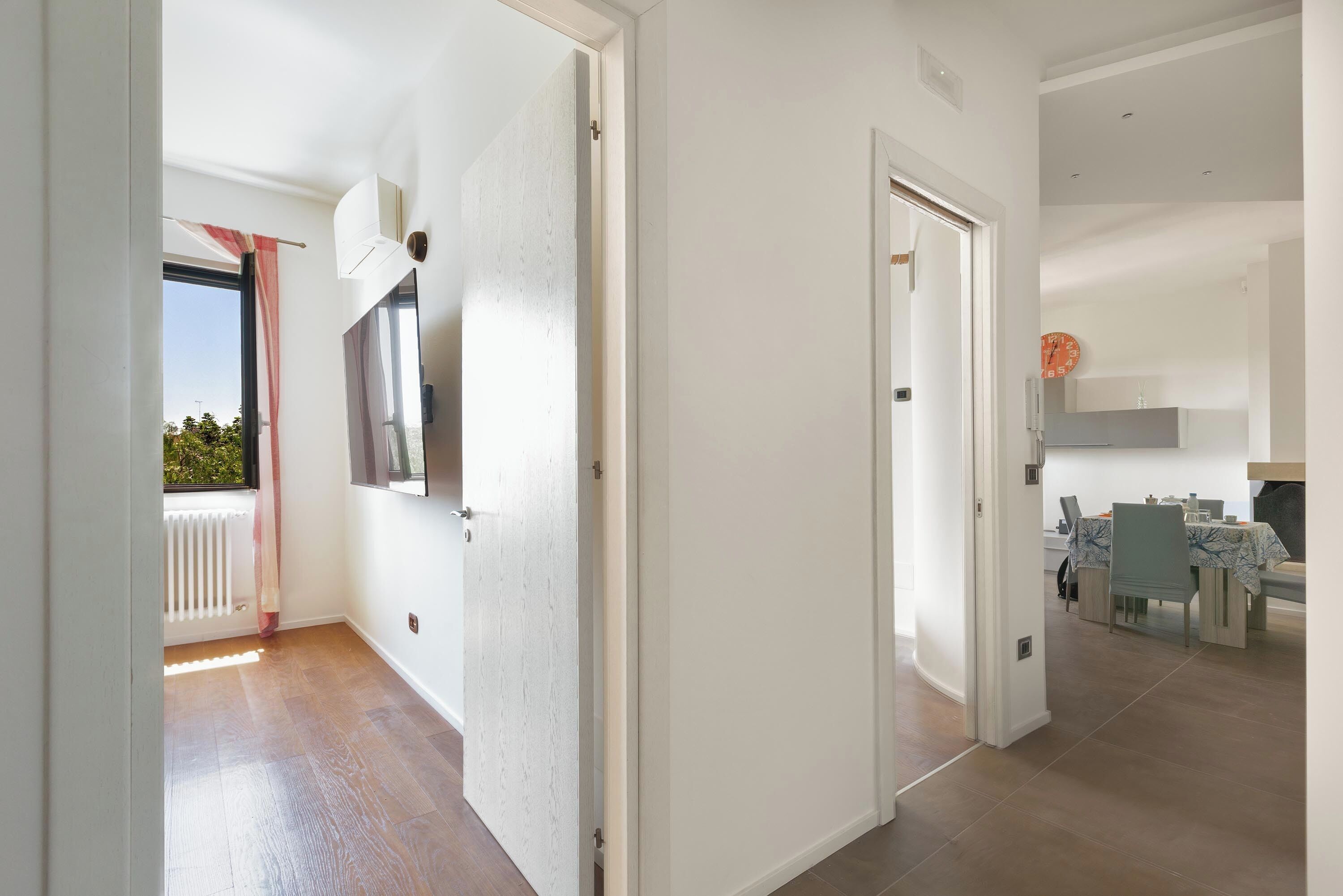 A modern interior with a dining area, a kitchen, and a view through an open door.