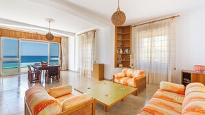 Amplia sala de estar con un sofá grande, una mesa de centro y un comedor con vista al mar.