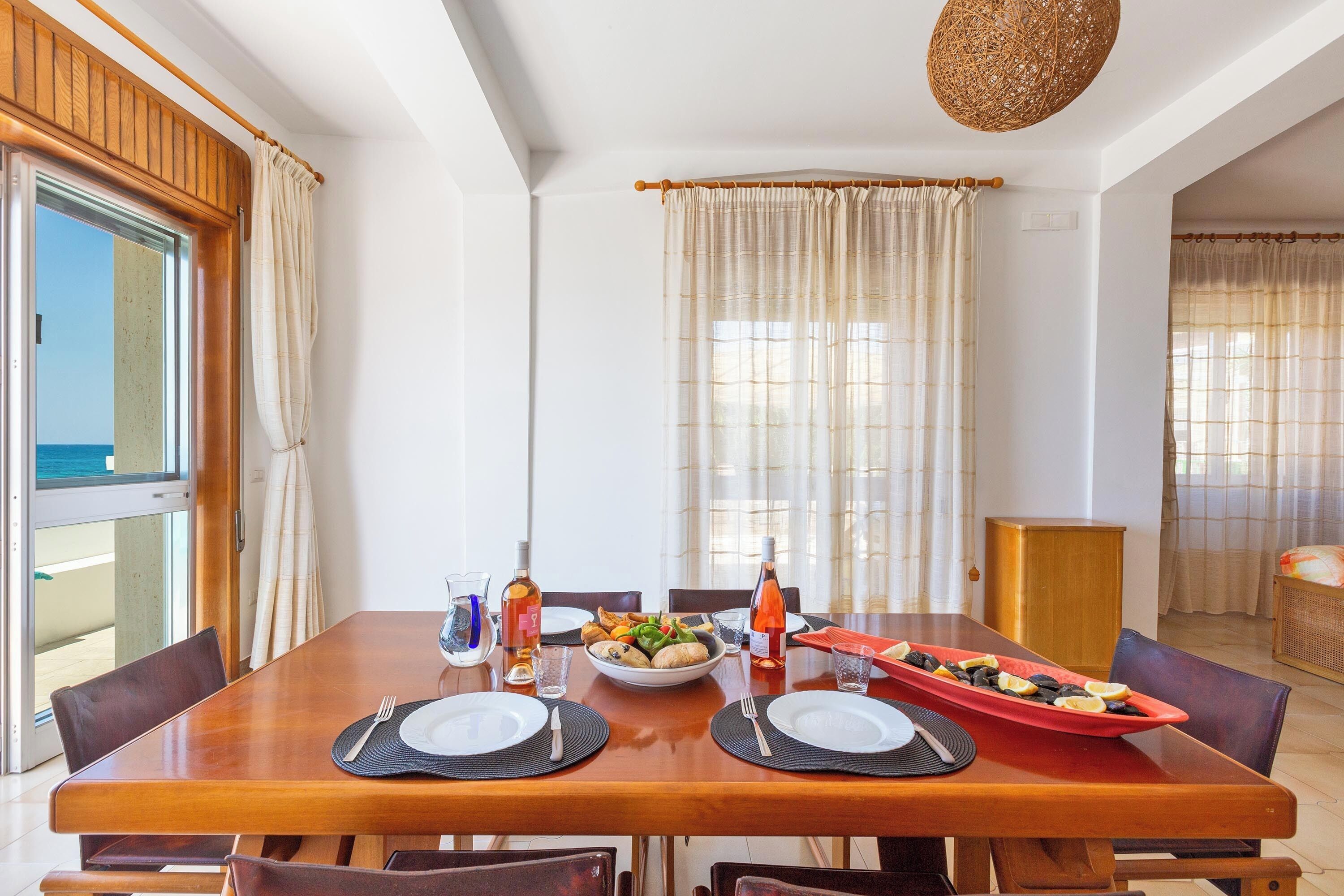 A dining area with a wooden table set for two, a bowl of fruit, and a red dish with lemons.