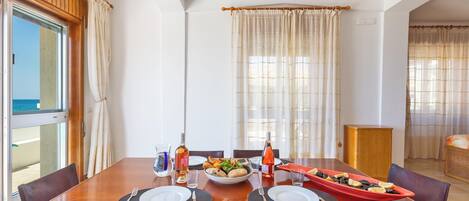 A dining area with a wooden table set for two, a bowl of fruit, and a red dish with lemons.